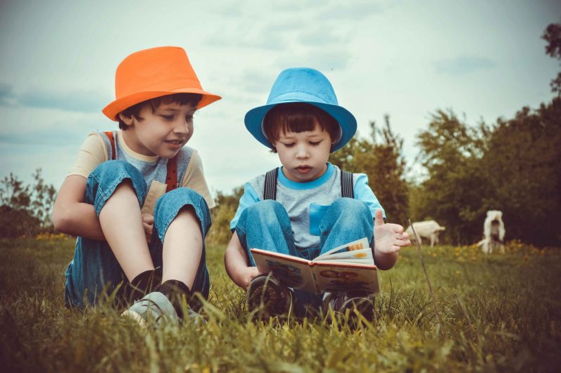 Deux enfants assis dans l'herbe qui lisent 