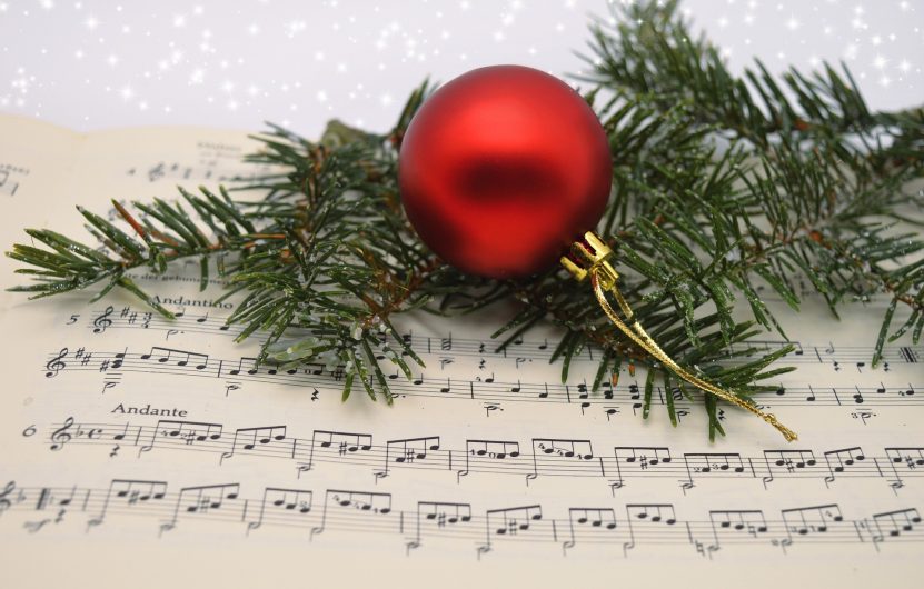 L’image représente une partition de musique avec une boule de noel et une branche de sapin posées dessus.